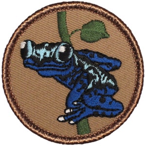 May include: Embroidered patch featuring a blue and black poison dart frog on a green branch with a green leaf. The patch is surrounded by a brown border.