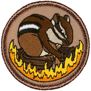 May include: Embroidered patch featuring a brown and white chipmunk sitting on a bed of orange flames. The patch has a brown border and is circular.