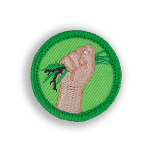 May include: Green embroidered patch with a hand holding a bunch of green grass. The patch has a green border.