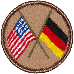 May include: A brown embroidered patch with a crossed American and German flag. The flags are red, white, and blue for the American flag and black, red, and yellow for the German flag.