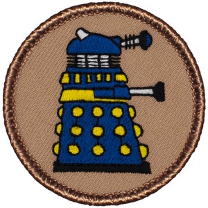 May include: A blue and yellow embroidered patch of a Dalek, a fictional robot from the British science fiction television series Doctor Who. The patch is circular and has a brown border.