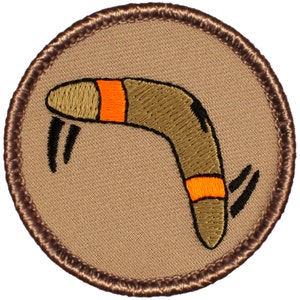 May include: A brown and orange embroidered patch with a boomerang design. The boomerang is flying through the air with a brown background.