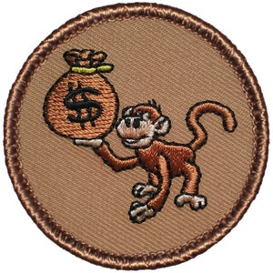 May include: A brown embroidered patch with a cartoon monkey holding a brown money bag with a dollar sign on it.