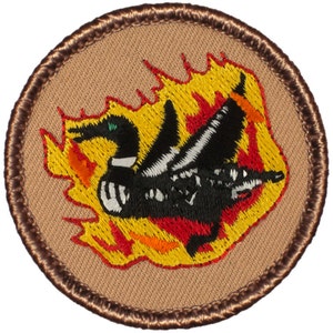 May include: A brown embroidered patch with a yellow, orange, and red flame design. A black and white loon is flying through the flames.