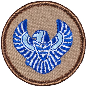 May include: A blue and white embroidered patch with a stylized eagle design. The patch is circular and has a brown border.