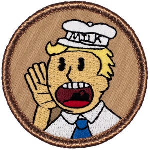 May include: Embroidered patch featuring a cartoon character with blonde hair, a white hat with the word "MILK", and a blue tie. The character is shouting with one hand raised. The patch has a brown border and background.
