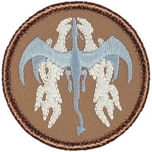 May include: Embroidered patch featuring a stylized, symmetrical design of a light blue dragon-like creature with outstretched wings and clawed limbs, set against a tan background. The patch has a brown border.