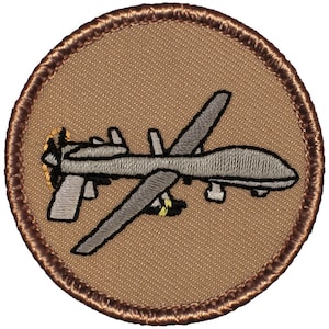 May include: A brown embroidered patch with a gray drone in flight. The drone has a propeller on the left side and a long, thin body.