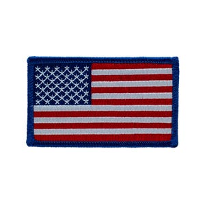 May include: A rectangular embroidered patch featuring the United States flag. The design includes a blue canton with white star-shaped stitching, alongside horizontal red and white stripes. The entire patch is bordered by a thick blue thread edge.