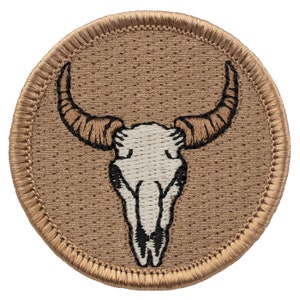May include: A brown embroidered patch with a white bull skull design. The patch has a brown stitched border.