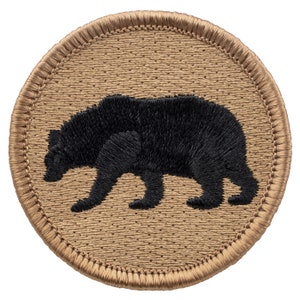 May include: A round, tan-colored patch with a black embroidered silhouette of a bear walking to the right.