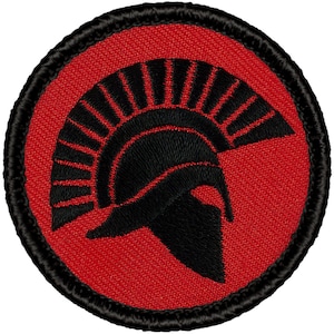 May include: A red embroidered patch with a black Spartan helmet design. The helmet is a profile view with a plume of feathers on top.