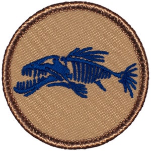 May include: A round, brown embroidered patch with a blue fish skeleton design. The fish is facing right and has a large mouth.