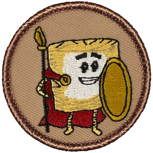 May include: A brown embroidered patch with a cartoon image of a smiling, anthropomorphic piece of toast holding a shield and a spear. The toast is wearing a red cape and has a gold crown on its head.