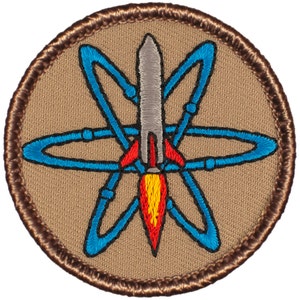 May include: A brown embroidered patch with a blue and gray rocket ship inside a blue atom symbol.