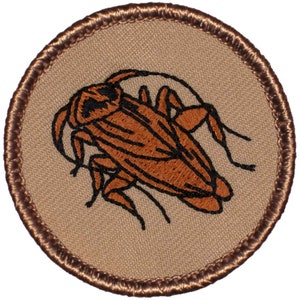 May include: A brown embroidered patch with a brown cockroach on a tan background. The patch has a brown stitched border.