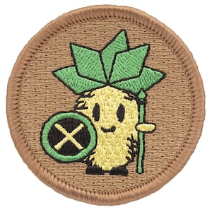 May include: A round, brown embroidered patch with a yellow pineapple character holding a green spear and a green shield with a black X. The pineapple has a green leafy crown.