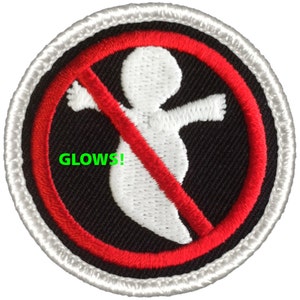 May include: A round, white-bordered patch with a red circle and a white silhouette of a ghost with a diagonal red line through it. The text "GLOWS!" is printed in green below the ghost.