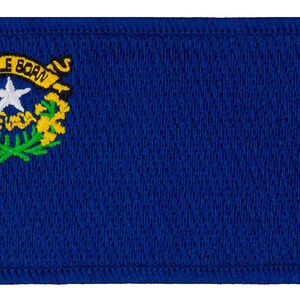 May include: A blue embroidered patch with the state seal of Nevada. The seal features a silver star with the word "Nevada" underneath, surrounded by a wreath of sagebrush and the words "Battle Born" on a ribbon.