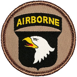 May include: A brown and tan embroidered patch with a black shield and a white eagle head. The shield has the word "AIRBORNE" in yellow letters above it.