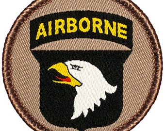 May include: A brown and tan embroidered patch with a black shield and a white eagle head. The shield has the word "AIRBORNE" in yellow letters above it.