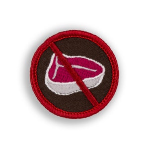 May include: A red and brown embroidered patch with a red line through a pink steak. The patch is a circle with a red border.