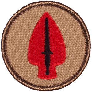 May include: A brown embroidered patch with a red and black arrowhead design. The arrowhead has a black dagger inside.