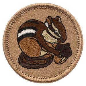 May include: A brown and white embroidered patch of a chipmunk holding a nut. The patch is circular and has a tan background with a brown stitched border.