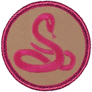 May include: A pink embroidered snake design on a beige fabric background. The design is surrounded by a pink border.