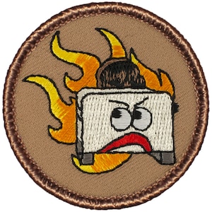 May include: A brown embroidered patch with a white toaster with a red mouth and angry eyes. The toaster is on fire with orange and yellow flames.