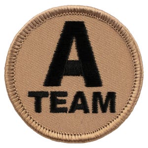 May include: A tan embroidered patch with black stitching. The patch is round and has the letter "A" in a large font with the word "TEAM" below it.
