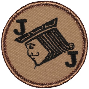 May include: A circular patch featuring a tan background with a black illustration of the Jack of Spades playing card. The patch has a brown stitched border and two black "J" letters. The Jack of Spades is depicted in profile.