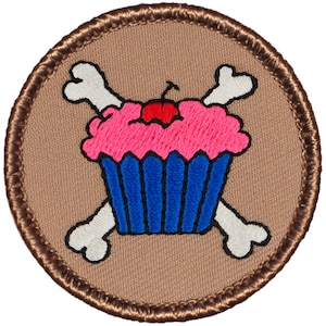 May include: A brown embroidered patch with a white cupcake with pink frosting and a red cherry on top. Two white bones are crossed behind the cupcake.