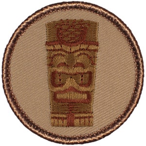 May include: A brown embroidered patch with a tan background featuring a tiki idol with a brown and red design.
