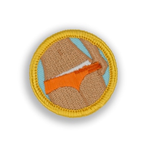 May include: A yellow embroidered patch with a tan outline. The patch features a cartoon image of a person wearing orange bikini bottoms.