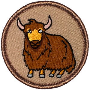 May include: A brown embroidered patch with a cartoon image of a brown yak with a white face and horns. The patch is circular and has a brown border.