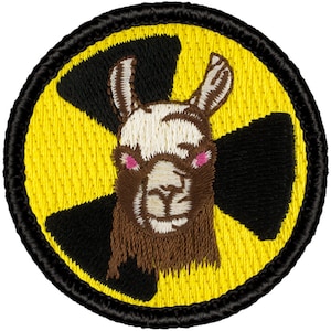 May include: A yellow and black embroidered patch with a llama's face in the center. The llama has brown fur, white fur around its eyes, and pink cheeks.