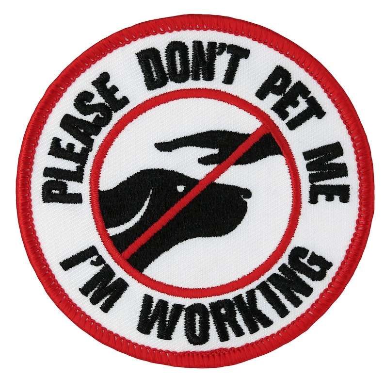 Puede incluir: Un parche bordado blanco y rojo con una silueta negra de la cabeza de un perro y una mano con una l&iacute;nea roja que la atraviesa. El texto en el parche dice "Please Don't Pet Me I'm Working".