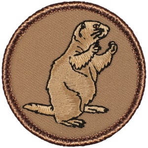 May include: A brown embroidered patch with a brown prairie dog standing on its hind legs. The patch has a brown stitched border.