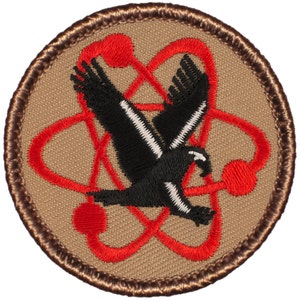May include: A brown and tan embroidered patch with a red atomic symbol and a black bird flying through it.