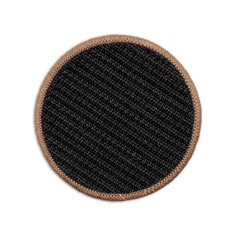 May include: A round black patch with a brown stitched border. The patch is made of a textured fabric.