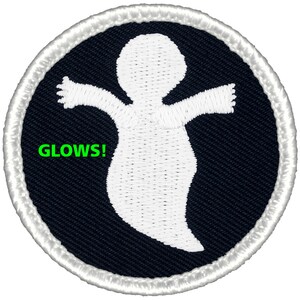 May include: A white ghost with outstretched arms on a black background with a white border. The text "GLOWS!" is written in green below the ghost.