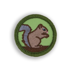 May include: A green and brown embroidered patch featuring a cartoon squirrel holding a nut.