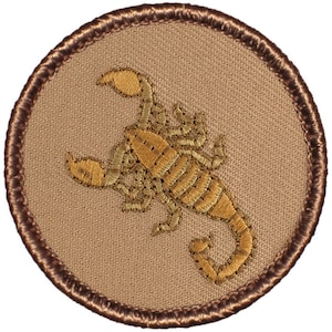 May include: Embroidered patch featuring a detailed scorpion design in shades of gold and tan. The scorpion is centered on a circular tan background, framed by a brown stitched border. Ideal for jackets, bags, or other fabric items.