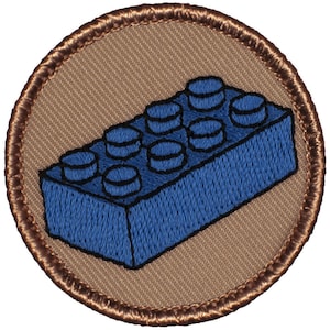 May include: A blue plastic toy building block with rounded edges and six studs on top. The block is surrounded by a brown fabric background.