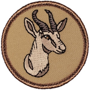 May include: Embroidered patch featuring a brown and white springbok antelope head with large horns. The patch is circular and has a brown border.