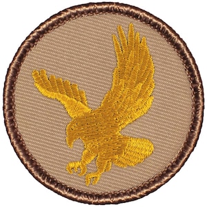 May include: A brown embroidered patch with a gold eagle design. The eagle is flying with its wings spread and talons extended.