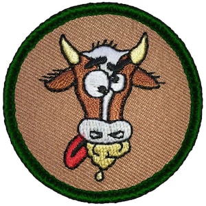 May include: A brown and white cartoon cow with a red tongue sticking out. The cow is wearing a green circle around its head. The cow is on a brown background.