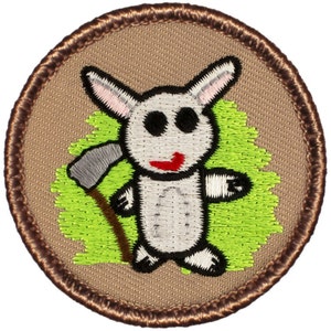May include: A brown embroidered patch with a white rabbit holding a silver axe. The rabbit has black eyes and a red mouth. The background is green.