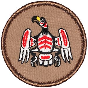 May include: A brown embroidered patch with a stylized eagle design. The eagle is black, white, and red with a yellow beak.